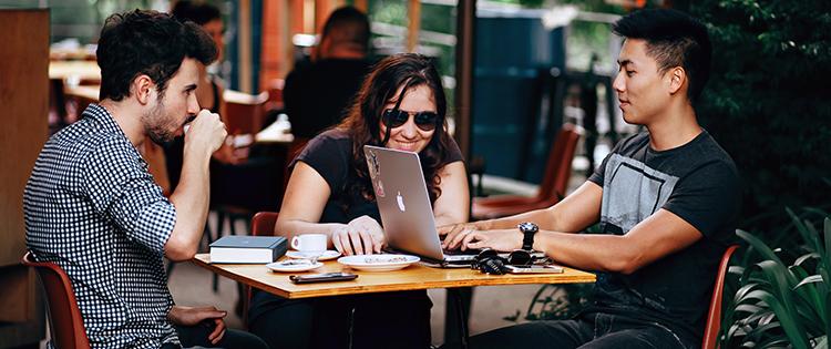 Friends drinking coffee outside and looking at a laptop