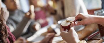 Photo of hands slicing an apple at a food-covered table surrounded by people