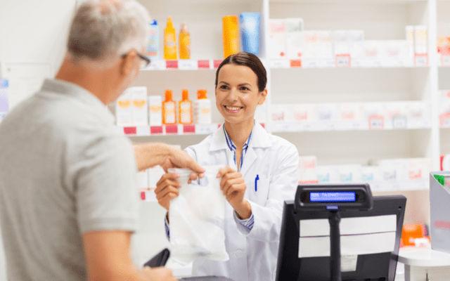 Photo of young female pharmacist handing a bag to an older man